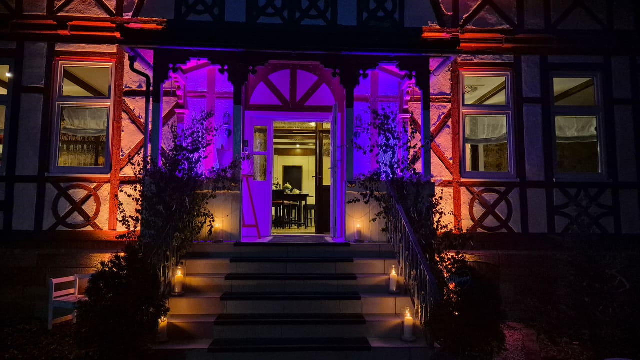 Fachwerkfassade des Schützenhauses Heldburg bei Nacht, lila und orange angestrahlt, Kerzen auf der Eingangstreppe